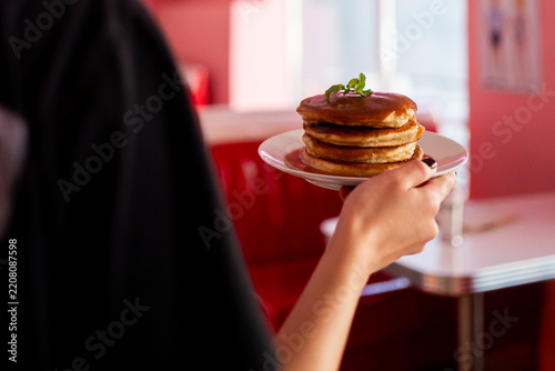 A person holding a plate with a stack of delicious pancakes topped with fresh mint in a retro diner setting.