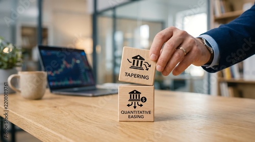 Businessman stacking wooden blocks with tapering and quantitative easing labels on office desk