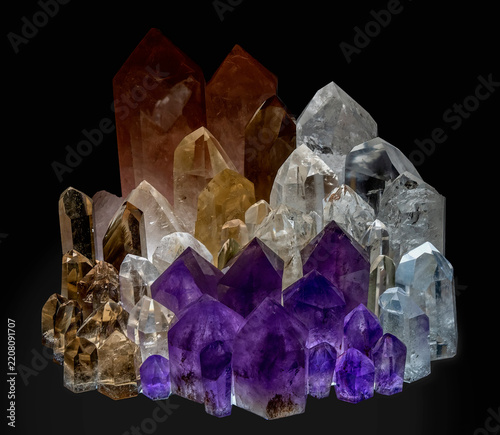 Collection of various illuminated quartz crystals—primarily rock crystal and amethyst—against a dark background.