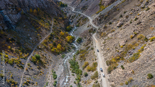 Aerial view of Sadpara Gol valley featuring a winding dirt road with vehicles, a flowing stream, and rugged rocky mountain slopes in Skardu, Gilgit, Pakistan.