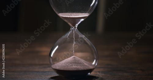 Hourglass with sand falling in super slow motion, evoking the passage of time, mortality, patience and the fleeting nature of life.