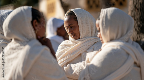 Ethiopian women gathered outside a community building in early morning light, a circle of friends animatedly sharing news in hushed voices with dramatic facial expressions,