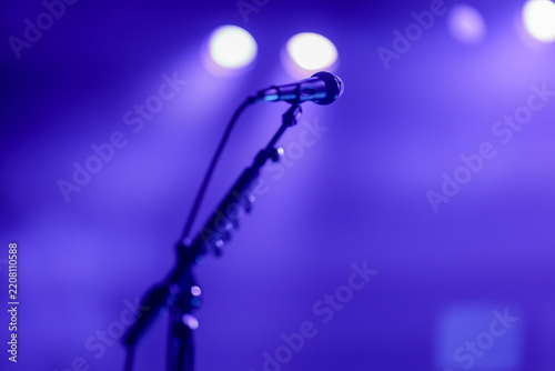 A microphone stands ready under dramatic blue stage lighting, in anticipation of a live concert performance by a singer singing in the mic.