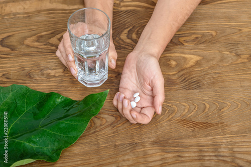 Pills and glass of water in woman's hands for daily use on wooden table, Adhering to treatment regimen