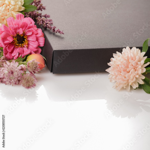Square gift box composition with pink, peach blooms, black gift box, white background, floral frame, copy space, elegant celebration design for birthday, wedding, anniversary, greeting card, template.