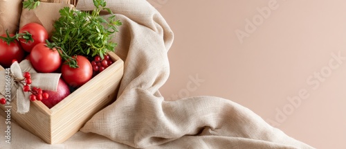 Close up wooden box of tomatoes and fresh herbs with draped linen on soft beige background for local food banner and website hero image