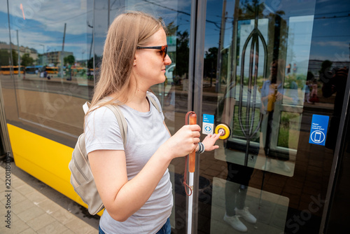 A blind woman with a white cane in her hand and dark glasses boarding the tram