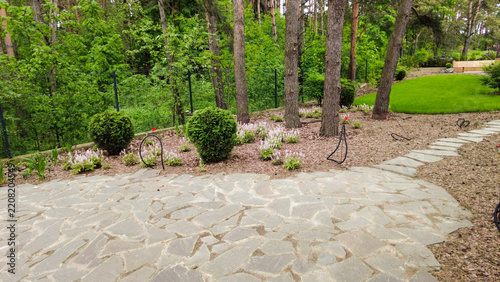 A scenic garden path featuring a stone walkway nestled among lush green trees, located in a tranquil residential area during daylight hours