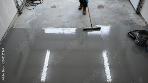 Person Using Roller Brush to Apply Grey Sealant or Coating on Garage Floor Surface