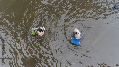Aerial view of two people wading through deep floodwaters carrying containers and fresh produce