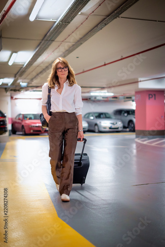Caucasian woman walking through modern underground parking garage with luggage and handbag