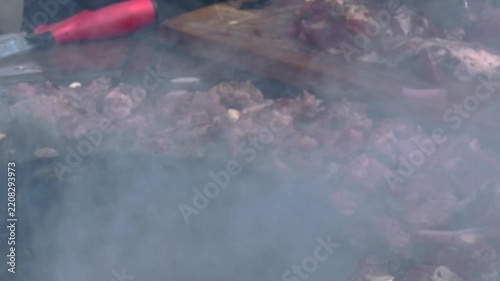 Juicy seasoned pork meat steaks and onions grilling on hot flat iron barbecue plate surrounded by dense white aromatic smoke during an outdoor culinary cooking event. 4K video.