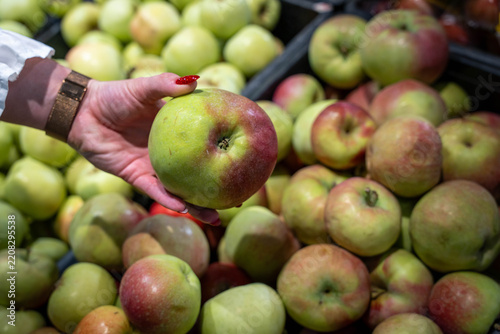 Obraz na plátně hand holding fresh ripe apple above grocery store crate during shopping trip ami