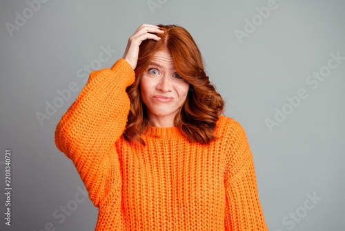 Woman in orange sweater looking confused and unsure with hand on head studio portrait