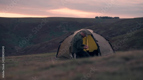 A man doing something inside his wild camping tent in the hills