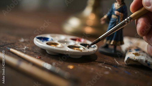 Artist's Hand Using Fine Detail Brush to Paint Miniature Figurine at Workstation