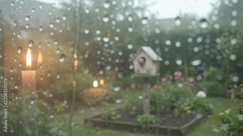 Raindrops on window pane with soft focus garden scene and lit candles, atmospheric weather