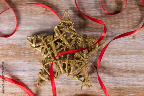 A golden Christmas star on a wooden background with a red ribbon