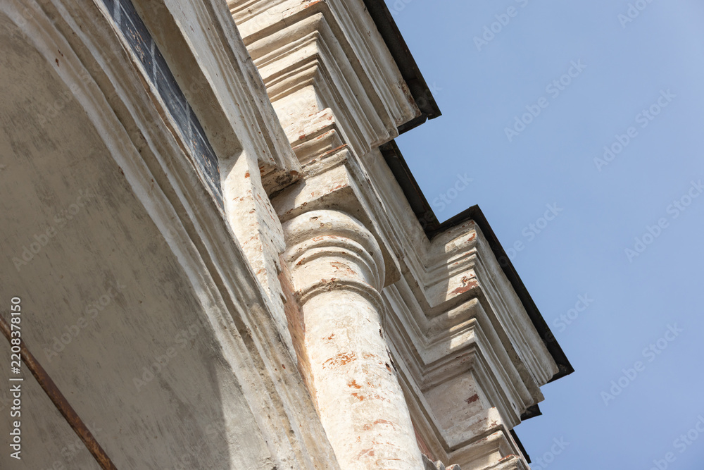 Obraz premium Old church facade featuring weathered stone columns, molded cornices and stucco ornamentation bathed in warm sunlight against a blue sky, emphasizing texture and classical architecture