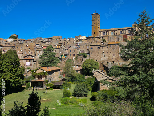 Scenic panoramic view of the ancient medieval town of Sutri with the Romanesque bell tower of Santa Maria Assunta Cathedral on a tufa cliff under a blue sky, Viterbo, Lazio, Italy