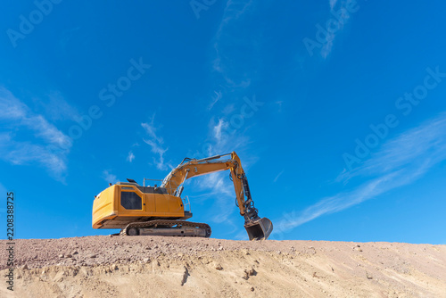 Bright yellow excavator on a crest of loose earth against blue sky with lots of copy space.