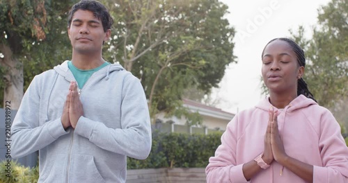 African American couple breathing, holding prayer pose in yard, meditating in hoodies smartwatch