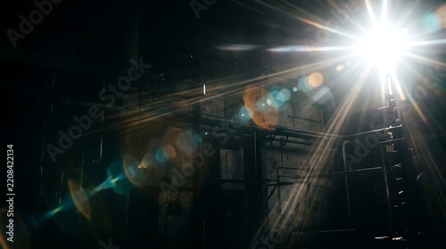 Bright white lens flare effect with anamorphic light streaks in a dark industrial factory setting