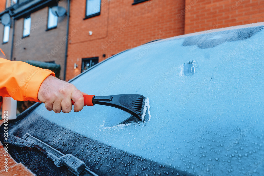 Fototapeta premium Person scraping ice off a car windshield in a residential area during winter morning