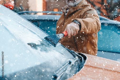 Man clears snow from car windshield on a winter day in the city