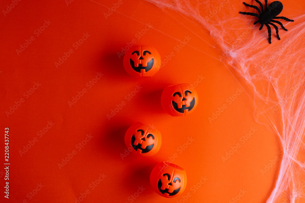 Fototapeta premium Top-down view of a Halloween background featuring pumpkin buckets and a spider on its web against an orange surface, with ample space for text