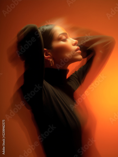 Artistic long exposure portrait of a beautiful woman with closed eyes wearing a black turtleneck sweater, posing against a warm orange gradient background.