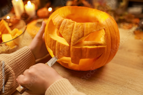 Person carving a scary pumpkin with a knife for a Halloween party. Hands making jack o lantern for autumn holiday decoration. Enjoy fun domestic preparation and festive traditions