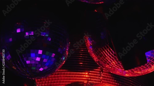 Disco Balls Scatter Red and Purple Reflections in a Dark Interior. Reflective spheres fill the dark interior while tiled mirror surfaces scatter changing light into colorful abstract patterns.