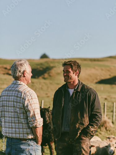 New Zealand family farming photography with father and adult son talking beside sheep pasture