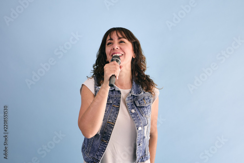 adult hispanic woman holding a microphone and singing in karaoke on blue background in Mexico Latin America, or latina and Mexican female portrait
