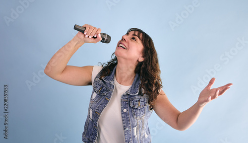 adult hispanic woman holding a microphone and singing in karaoke on blue background in Mexico Latin America, or latina and Mexican female portrait