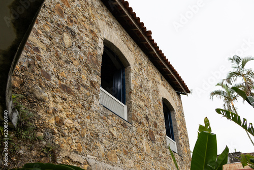 Low-angle view of stone building. Arched windows, blue frames, clay tiles.
