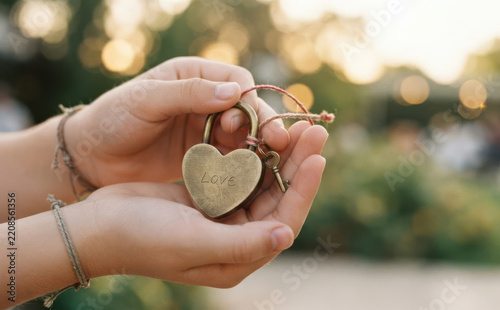 Close-up of caucasian young woman holding a bronze heart shaped love lock with key in hands