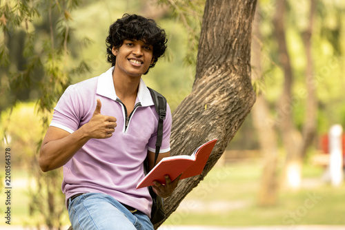 Portrait of indian young college student with backpack and notebooks standing and smiling in park