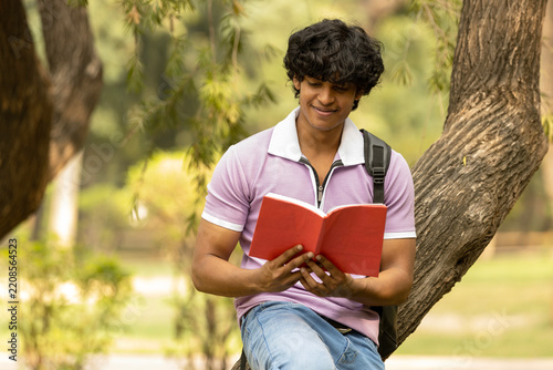 Portrait of indian young college student with backpack and notebooks standing and smiling in park