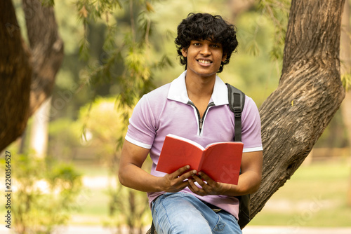 Portrait of indian young college student with backpack and notebooks standing and smiling in park