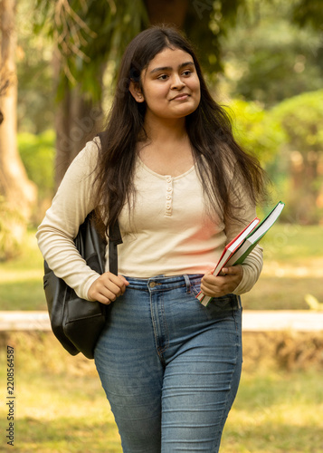 Portrait of indian young girl college student with backpack and notebooks standing and smiling in park