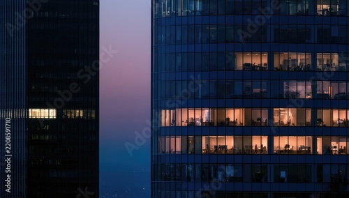 Modern glass office building facade with illuminated office windows at night.