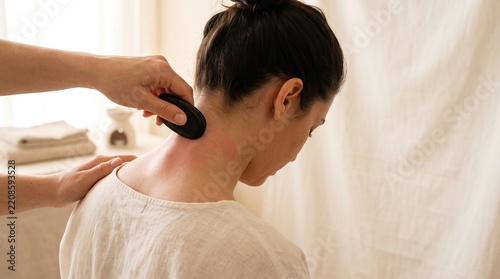Therapist performing traditional Gua Sha scraping massage on woman neck at luxury wellness spa