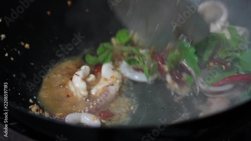 4K Chef stir-frying fresh squid rings with crushed red chilies and garlic in a hot wok, cooking process for spicy Thai stir-fried squid with holy basil concept.