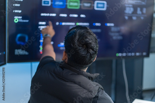Rear view of a programmer pointing at software code displayed on multiple monitors in a modern technology workspace, representing programming, software development, and digital innovation.