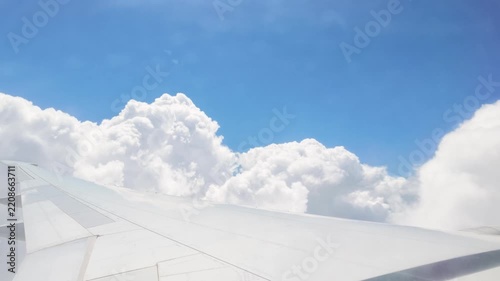 4K 60fps POV shot from a passenger airplane window showing the aircraft wing flying close to and momentarily passing through large, bright white cumulus clouds against a blue sky over Istanbul.