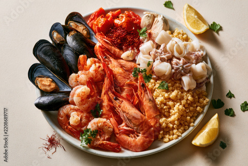 Mediterranean seafood ingredients with prawn, mussel, squid, tomato, saffron, garlic, lemon and pasta arranged on a ceramic plate for gourmet cooking.