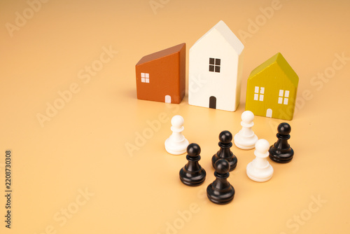 Obraz na plátně Miniature houses surrounded by black and white chess pieces representing real estate competition, property strategy, market rivalry and home investment decisions