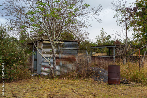 Dilapidated rural shack and rusty barrel in a dry countryside landscape. Queensland, Australia.